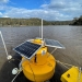 Yellow water quality monitoring buoy floating on water in lake.