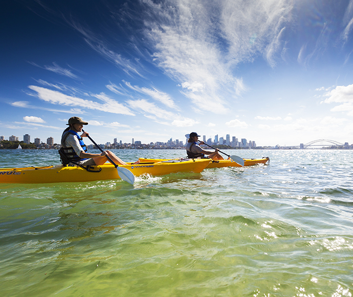 People wearing sunhats, sun protection, paddling their kayaks off Bradleys Head near the city of Sydney