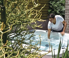 A man checks the water temperature in his outdoor spa bath.