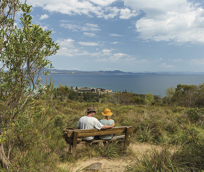 Couple sitting on a bench seat at a lookout, Monument track, Arakoon National Park