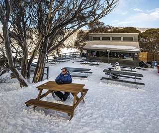 Tourist sitting at an outdoor table at the Alpine Eye cafe, Perisher Valley, in winter