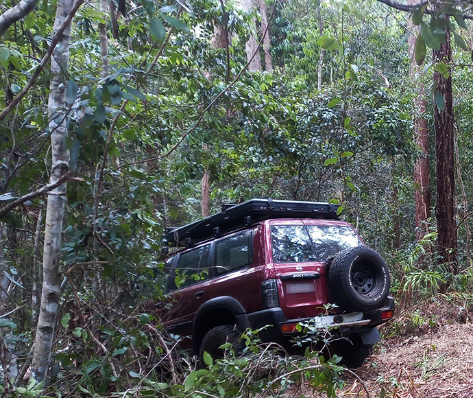 Maroon 4WD parked down slope off road.