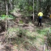 A dirt trail through a forest; a person in high-vis gear and a yellow sign that says 'no entry'