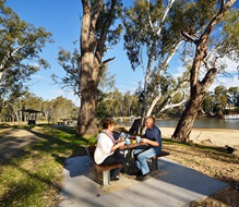 Two people enjoying a sunny picnic table beside a river