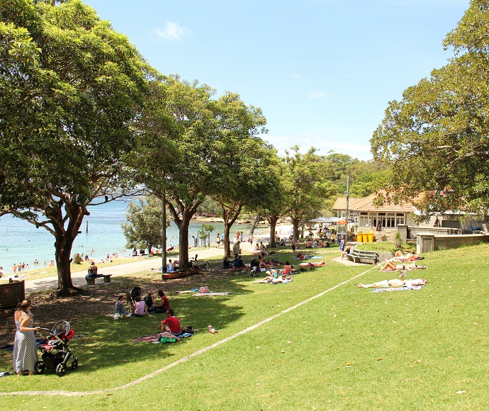 People picnicking on a grassy area in Nielsen Park alongside Shark Bach with buildings in the background. 