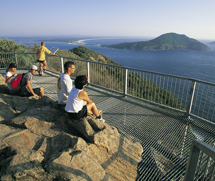 People sitting at Tomaree Head lookout, Tomaree National Park, Port Stephens. Views to Yacaaba Head and Cabbage tree island.