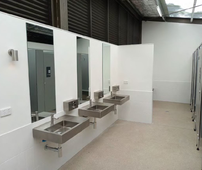 3 sinks, 3 mirrors and 3 wall-mounted soap dispensers with toilet cubicle doors reflected in mirrors