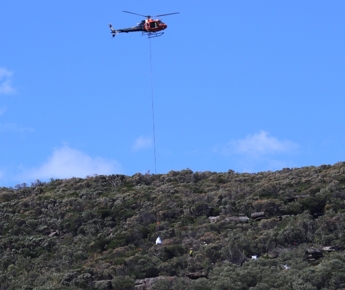 A helicopter lifts tools and equipment to a NPWS work site.