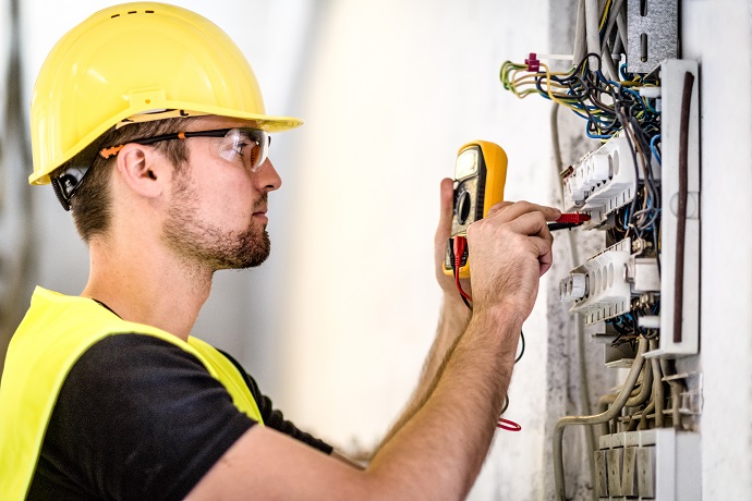 Man wearing yellow hardhat checking electrical wiring.