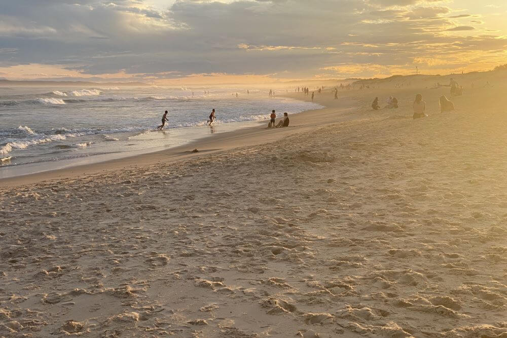 Silhouettes of people walking on the beach while the sky turns brilliant shades of orange, blue and grey as the sun sets