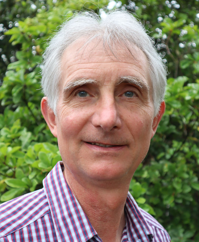 Martin Fallding has grey hair and blue eyes standing in front of a hedge.