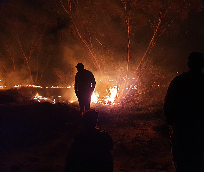 Man standing in a park at night with backburning going on behind him