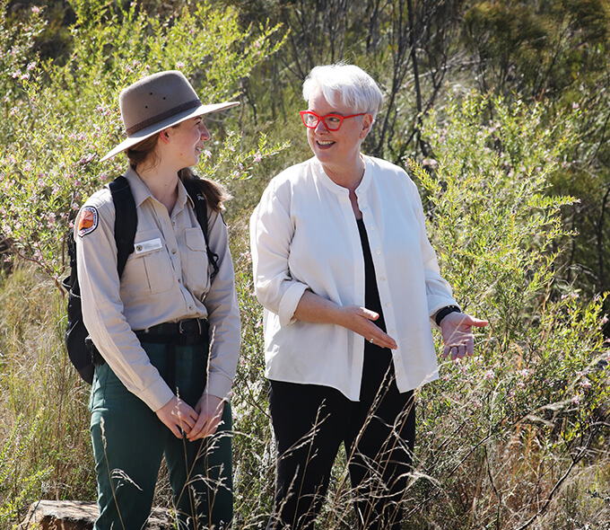 Minister Sharpe standing next to native shrubs talking to a National Parks staff member