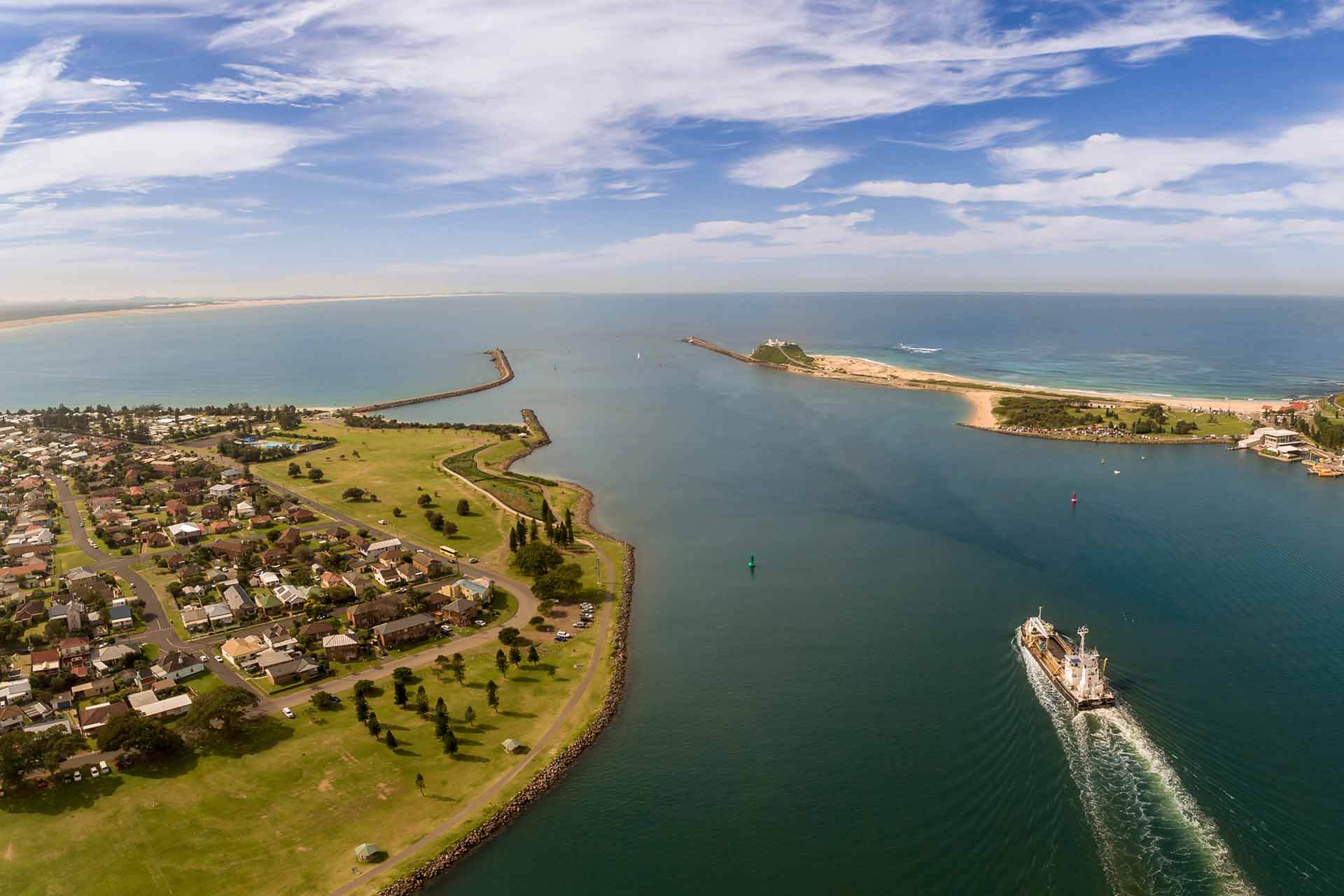 Aerial view of a coastal town with a ship entering a channel between 2 breakwaters