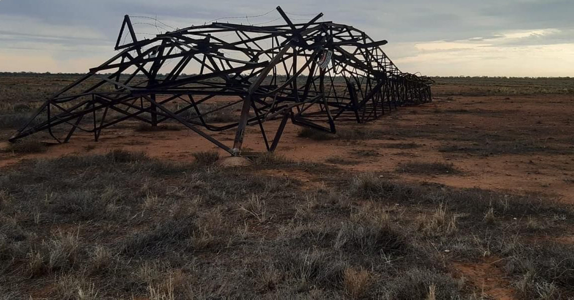 A metal transmission tower lies crumpled on the ground