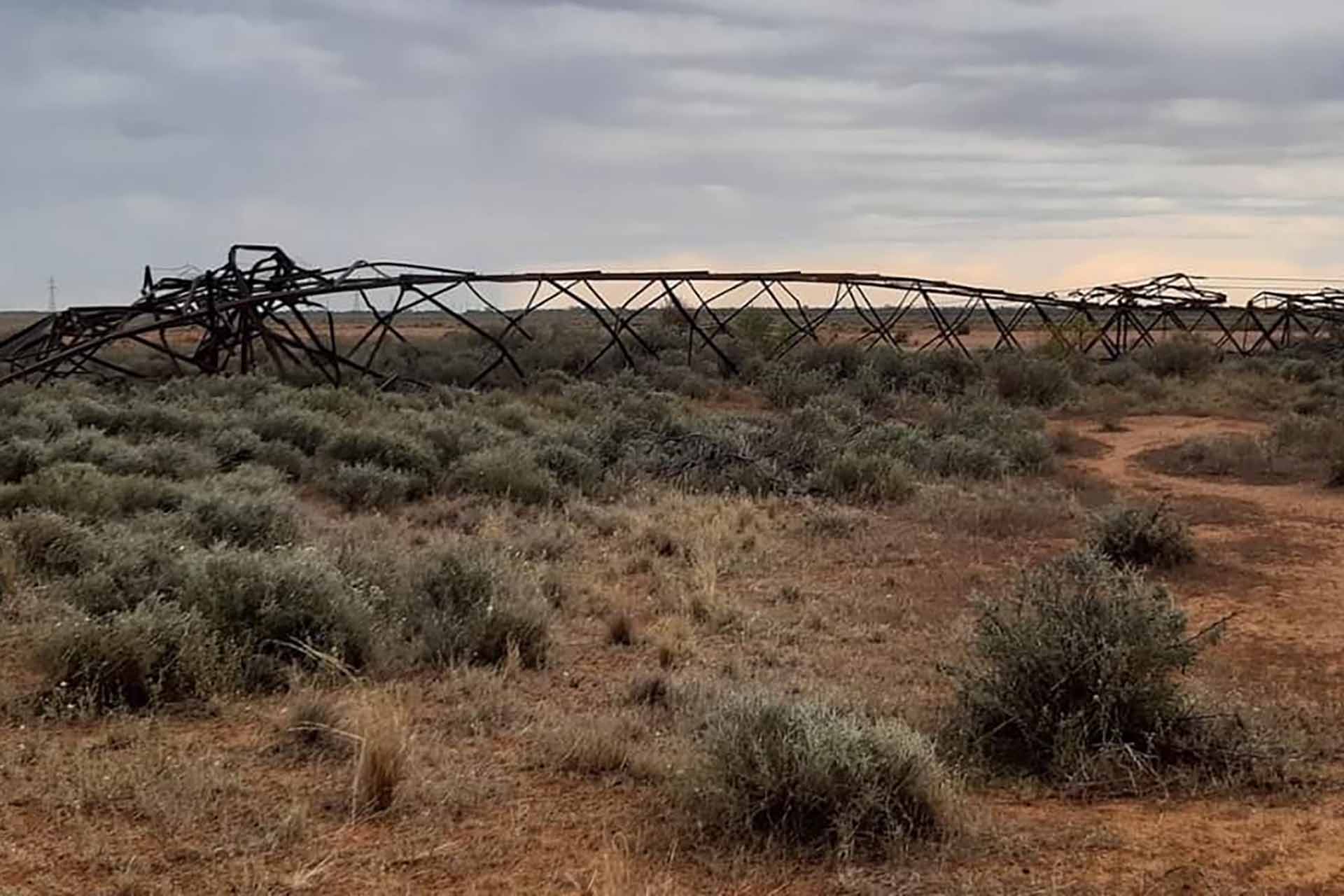 A metal transmission tower lies crumpled on the ground