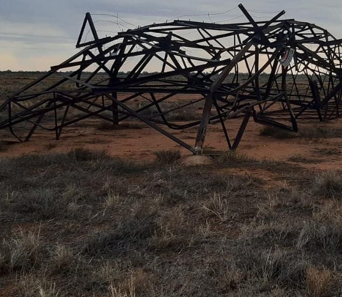 A metal transmission tower lies crumpled on the ground