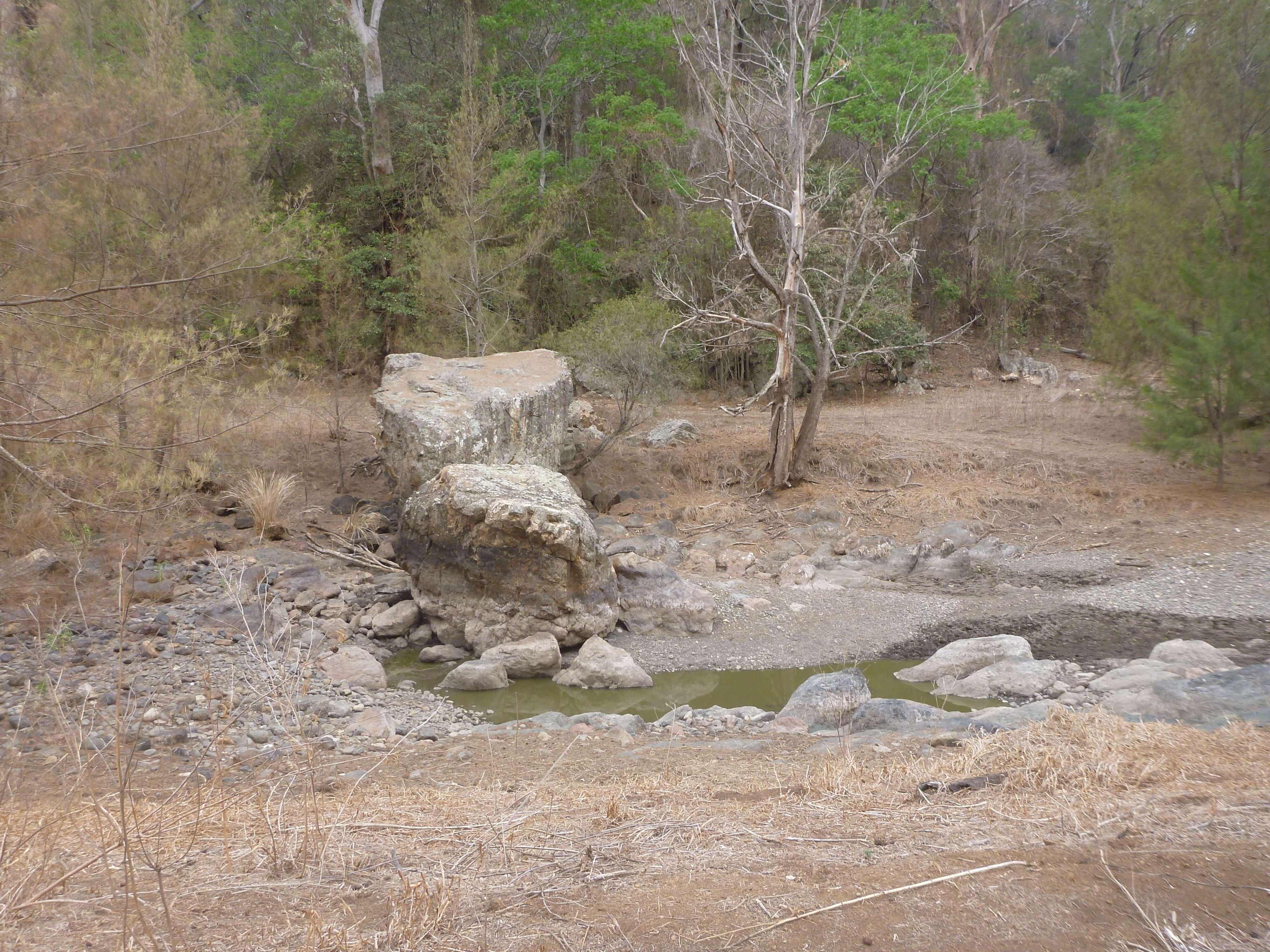 A small waterhole with minimal water, surrounded by dry, rocky terrain and sparse vegetation in Barnard River, Curracabundi National Park, illustrating the impact of drought.