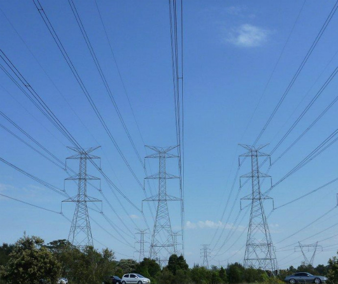Three large electricity towers and electricity lines against a blue-sky background.