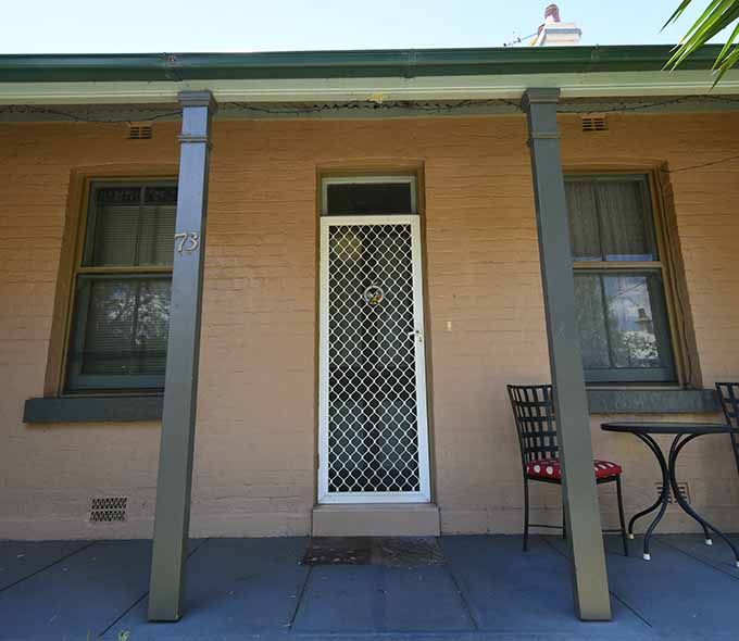 The front of a yellow cottage with screen door and chairs in front