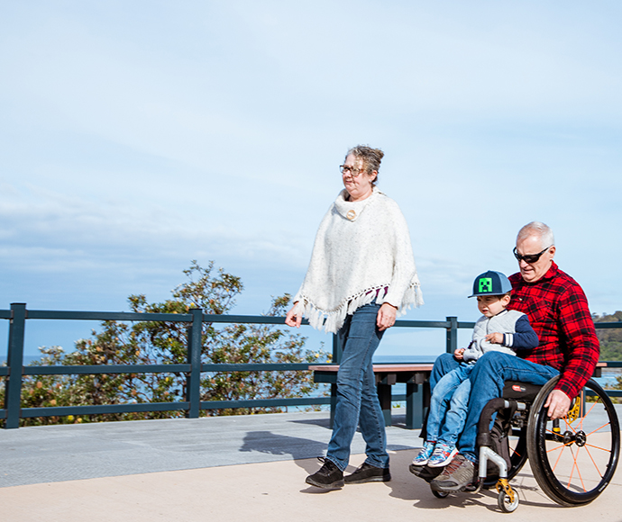 Woman walking next to a man in a wheelchair with a child on his lap.