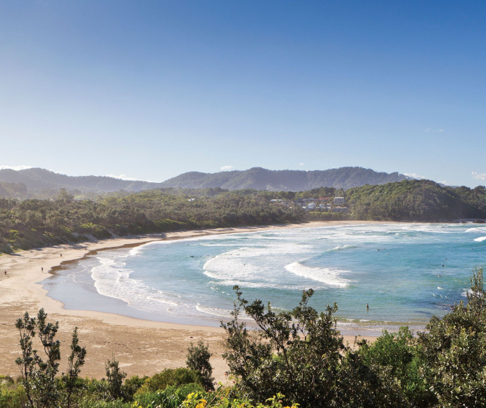 Looking down on the turquoise blue water of Diggers Beach with hills to the north and a clear blue sky above.