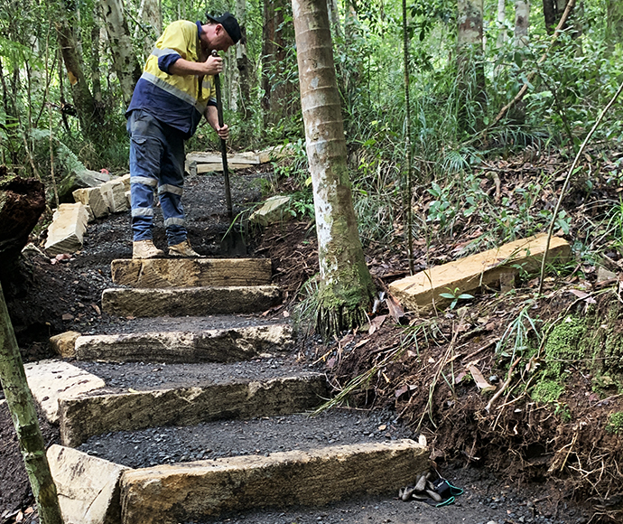Person constructing stone steps in a forested area.