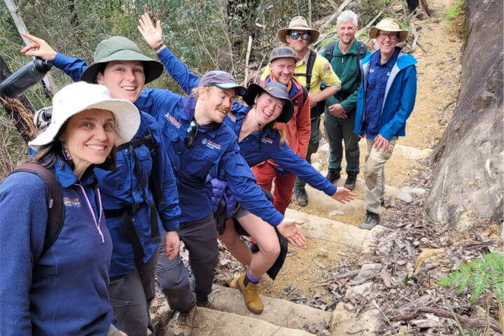 A group of 8 mostly smiling people on a dirt path