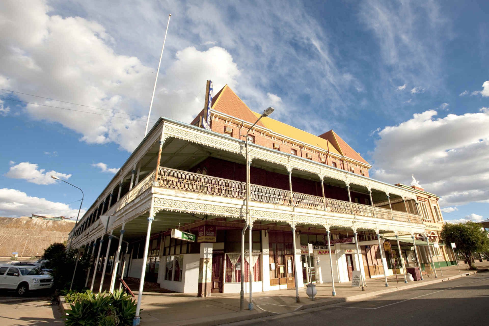 A large turn of the 19th/20th century hotel with slender pillars and an ornate wrap-around patio on the first floor