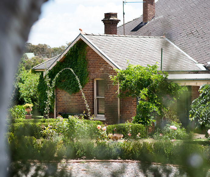 Charming brick cottage with a lush garden. Ivy climbs the walls, a curved trellis adds elegance. Private, peaceful atmosphere with blooming flowers.