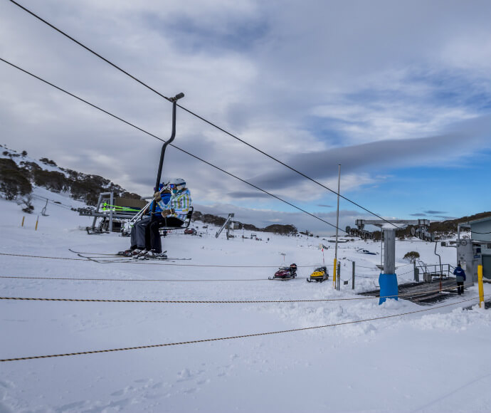 Skiiers riding a t-bar chair lift up a snow-covered hill.