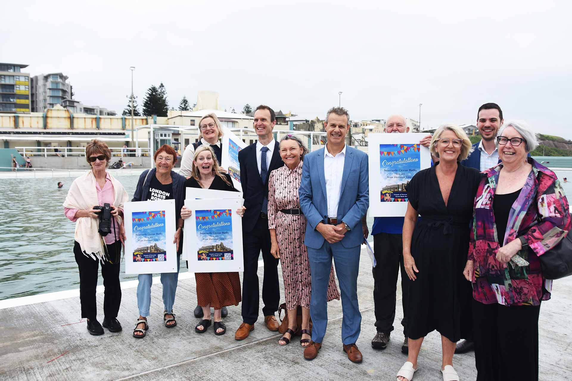 A group of smiling people posing beside pool, holding posters