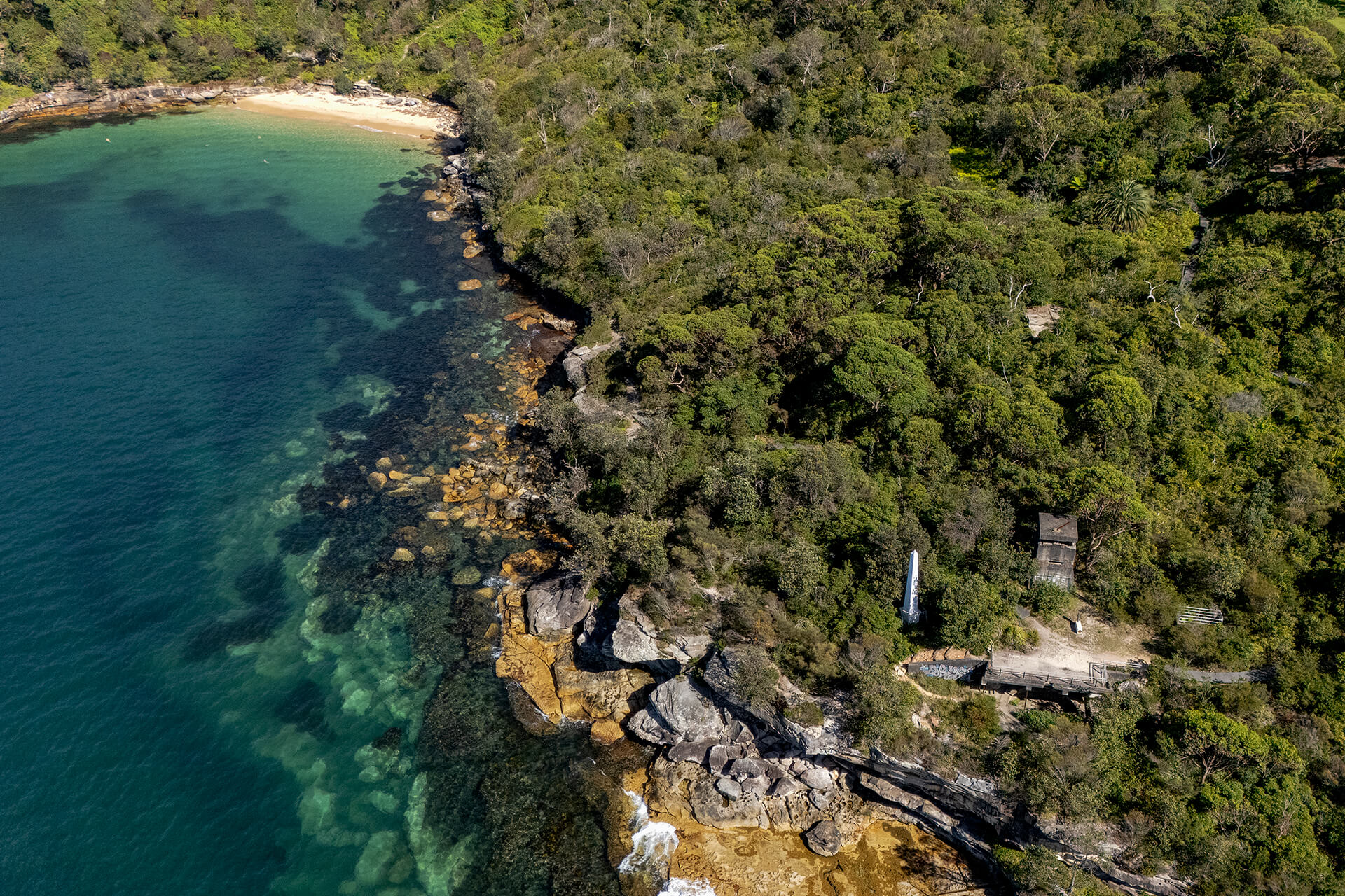 Aerial view of concrete structures amongst trees, azure coastline and beach nearby