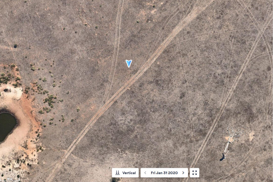 An aerial photograph of a barren-looking landscape around some dirt roads, with a smattering of greenery close to a creek