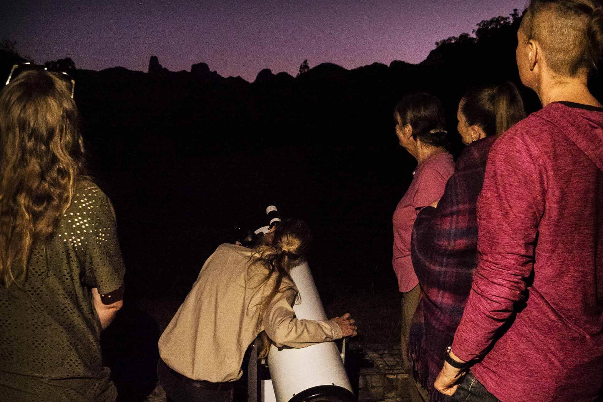 People watching a dark sky, one girl looking through a telescope