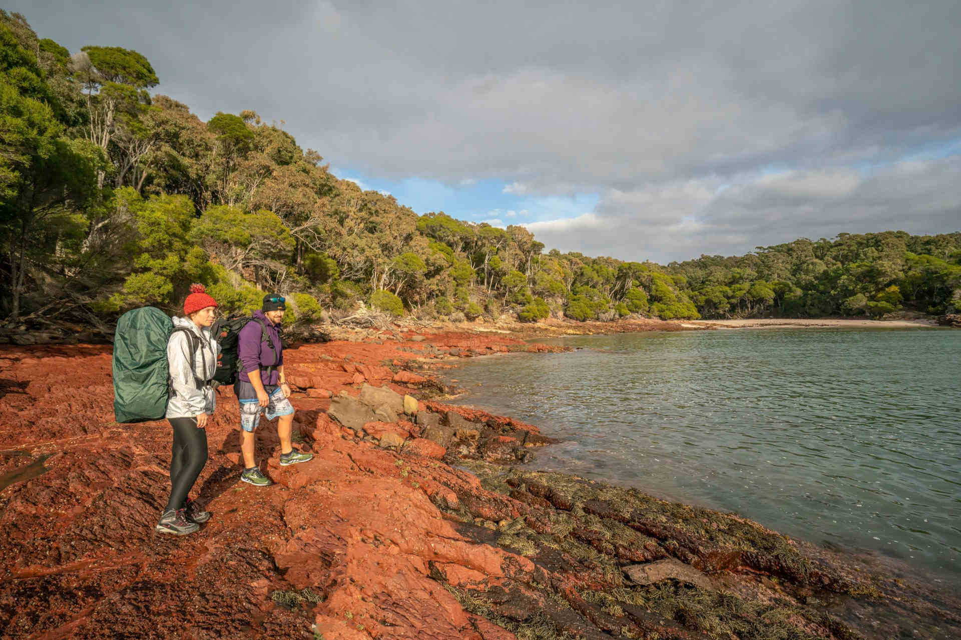 Two bushwalkers standing on a rocky ledge looking out over Bittangabee Bay.
