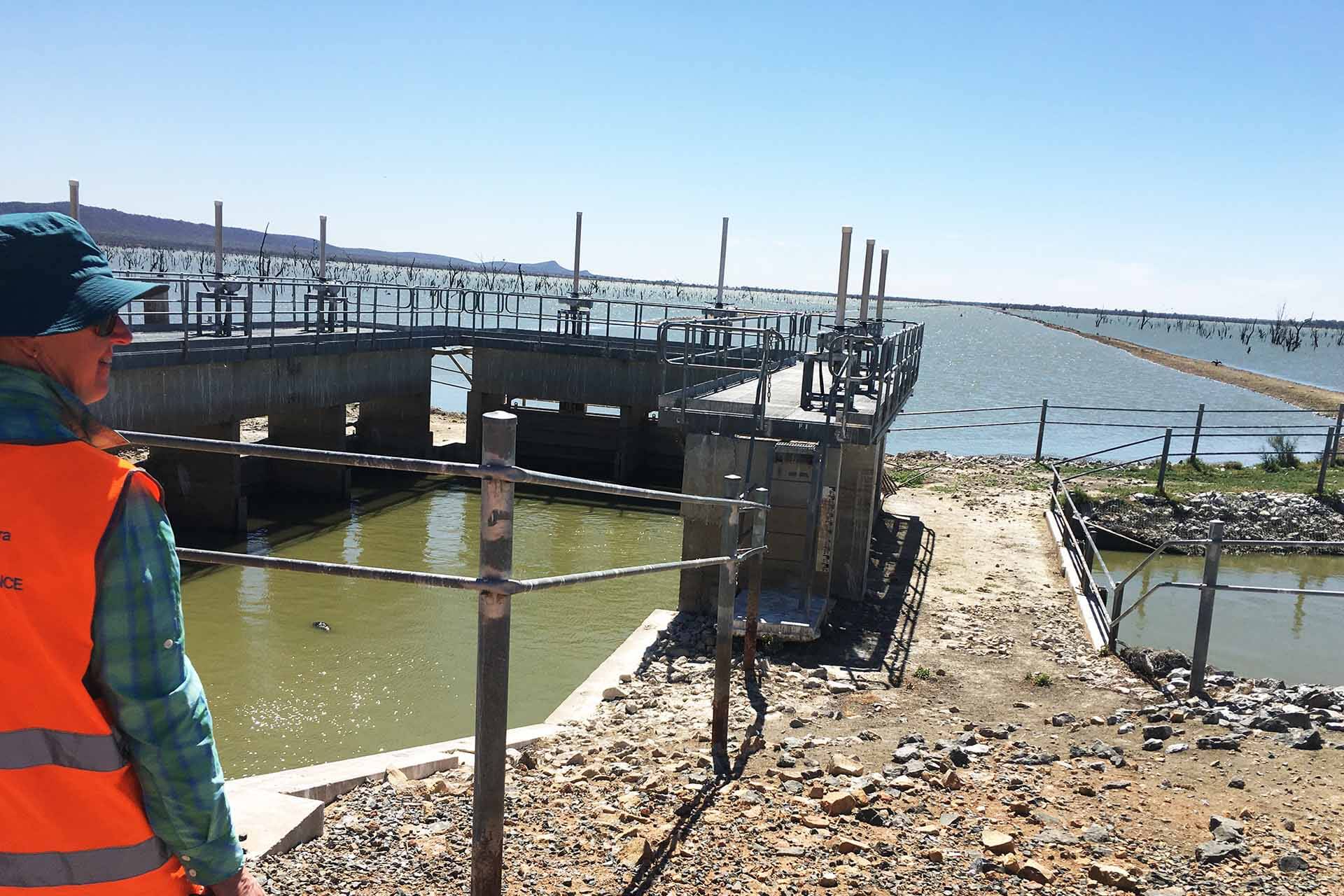 A man in high vis looks over a lake and infrastructure.