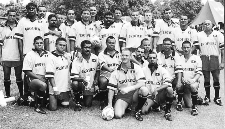 Black and white group photo of 25 Brothers football players, possibly taken in 1999. The team is arranged in two rows, with some players standing in the back and others kneeling in the front. All are wearing white short-sleeved football jerseys with 'Brothers' printed on them, along with dark shorts and knee-high socks.
