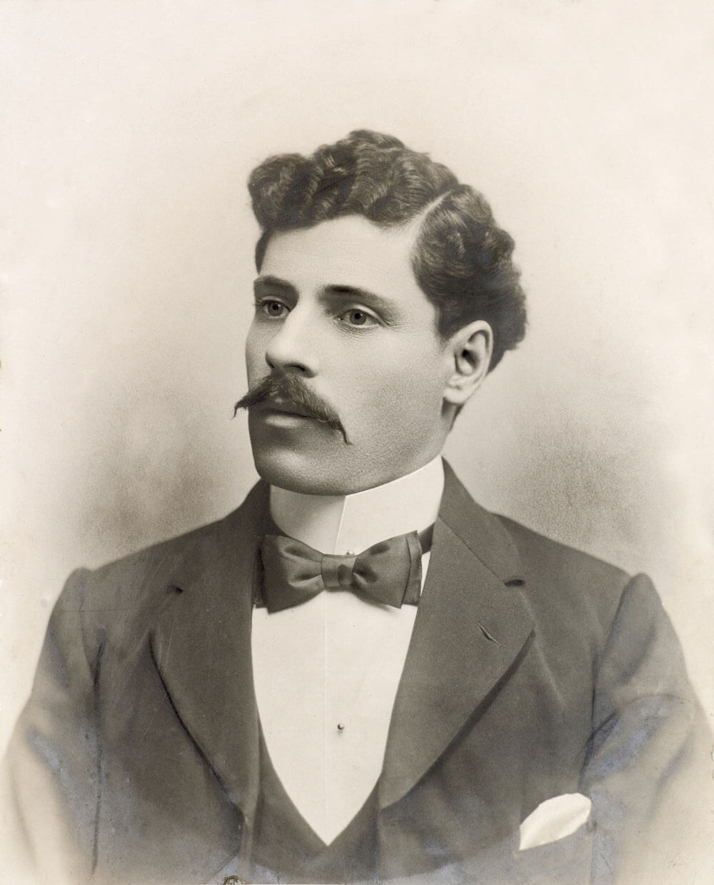 Portrait of Betro Abicare, circa 1902. He is seated, wearing a three-piece suit with a bow tie. He has short curly hair, a moustache, and is gazing to the left. The formal attire and composed pose reflect early 20th-century portrait style.