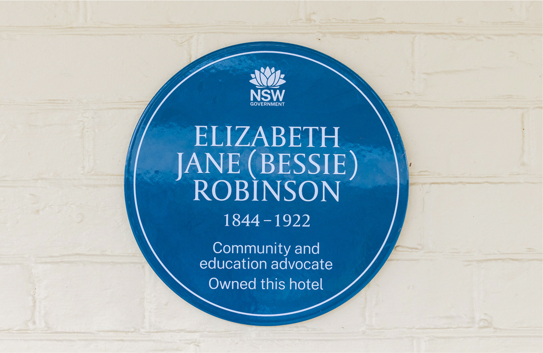 Blue Plaque commemorating Elizabeth Jane (Bessie) Robinson, mounted on a brick wall. The plaque reads: 'Community and education advocate. Owned this hotel,' recognizing her contributions to local society and her role as a hotel owner.