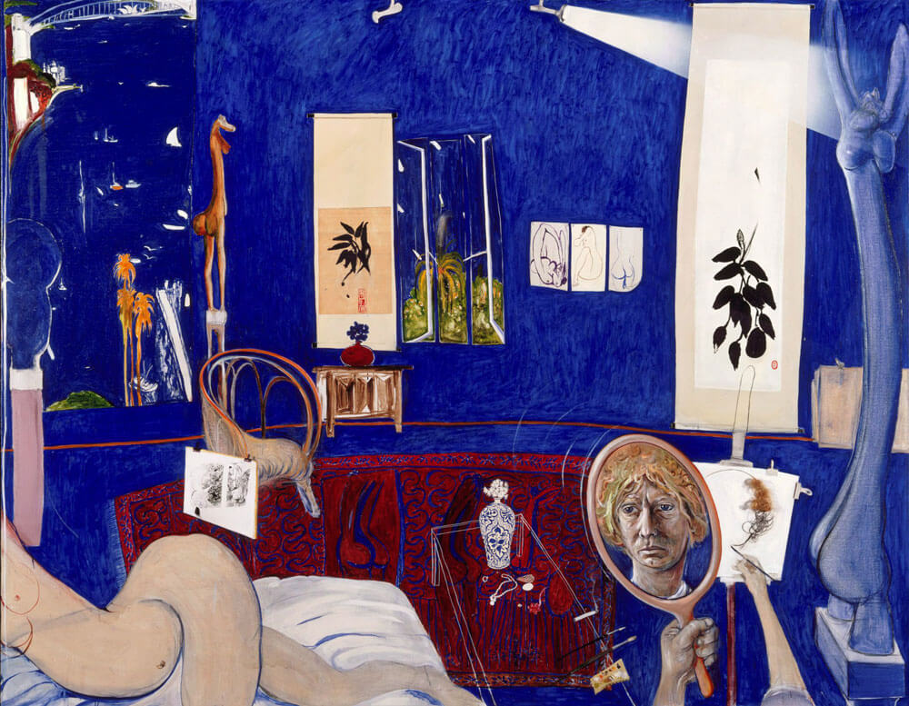 Self-portrait in the Studio, 1976, by Brett Whiteley. A richly detailed interior scene dominated by sweeping curves, warm textures, and the deep Ultramarine blue of Sydney Harbour visible through the window. A small mirror on the right reflects Whiteley's self-portrait, subtly integrated into the composition. The studio is filled with eclectic objects, evoking both luxury and introspection, with hints of Eastern influence and a sense of psychological tension beneath the surface.
