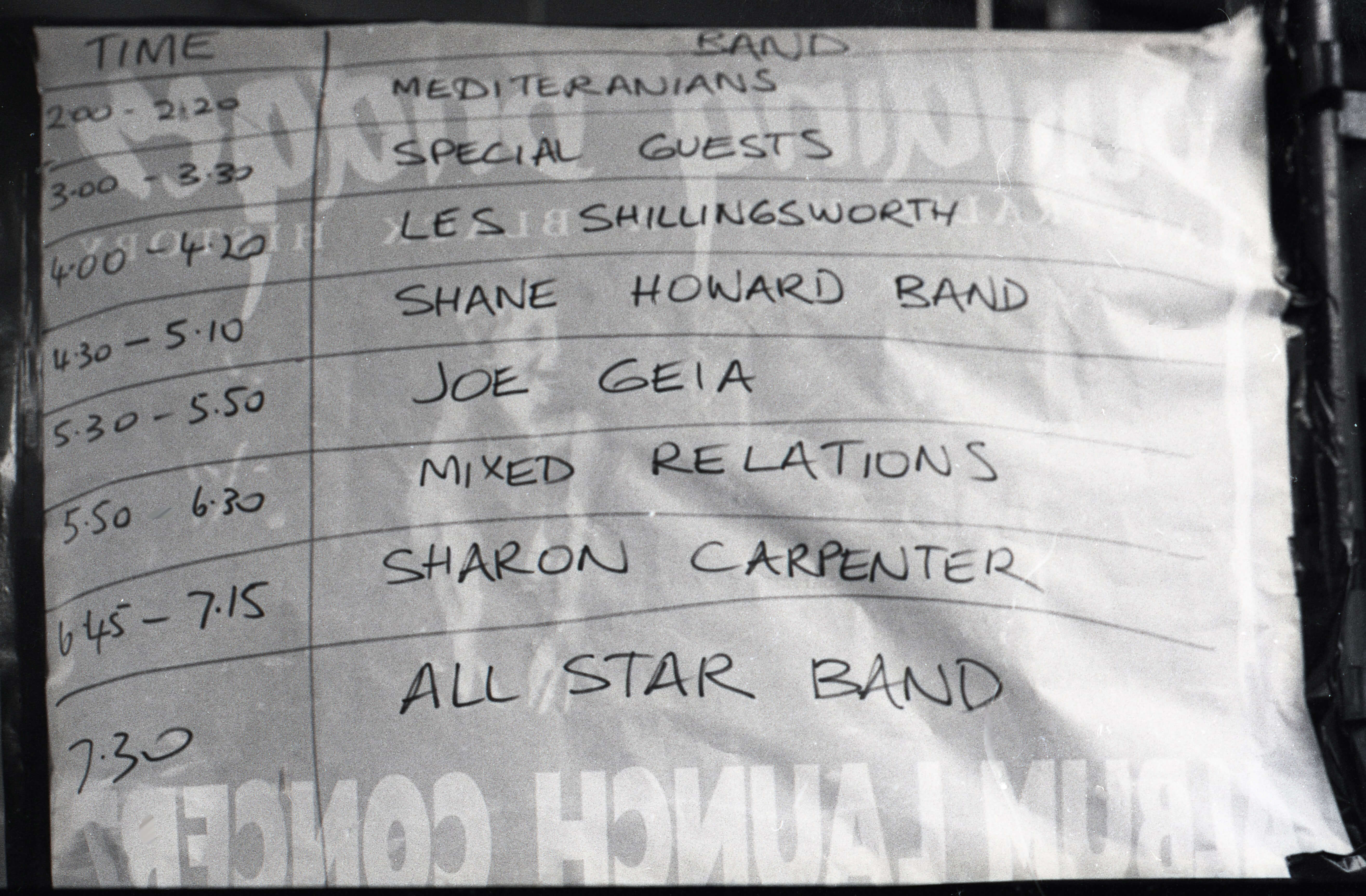 Black and white photo of the handwritten setlist from the 1989 Building Bridges Concert. The setlist is drawn as a table with two columns and nine rows. The header row reads 'Time' and 'Band'. The left column lists time slots from 2:00pm to 7:30pm, while the right column names the performing bands scheduled for each time.