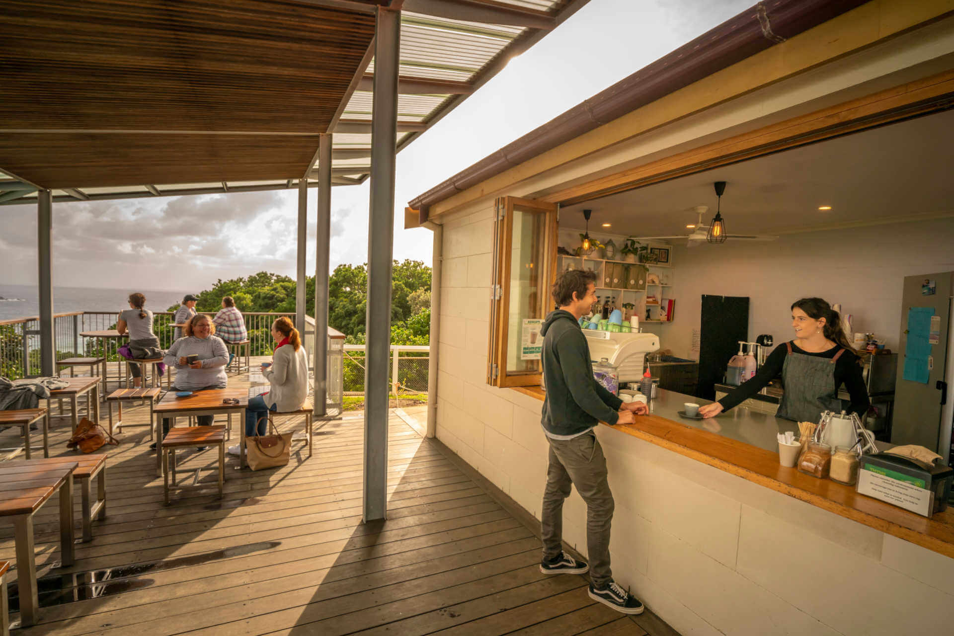 Coastal cafe with outdoor deck, serving customers overlooking ocean and trees