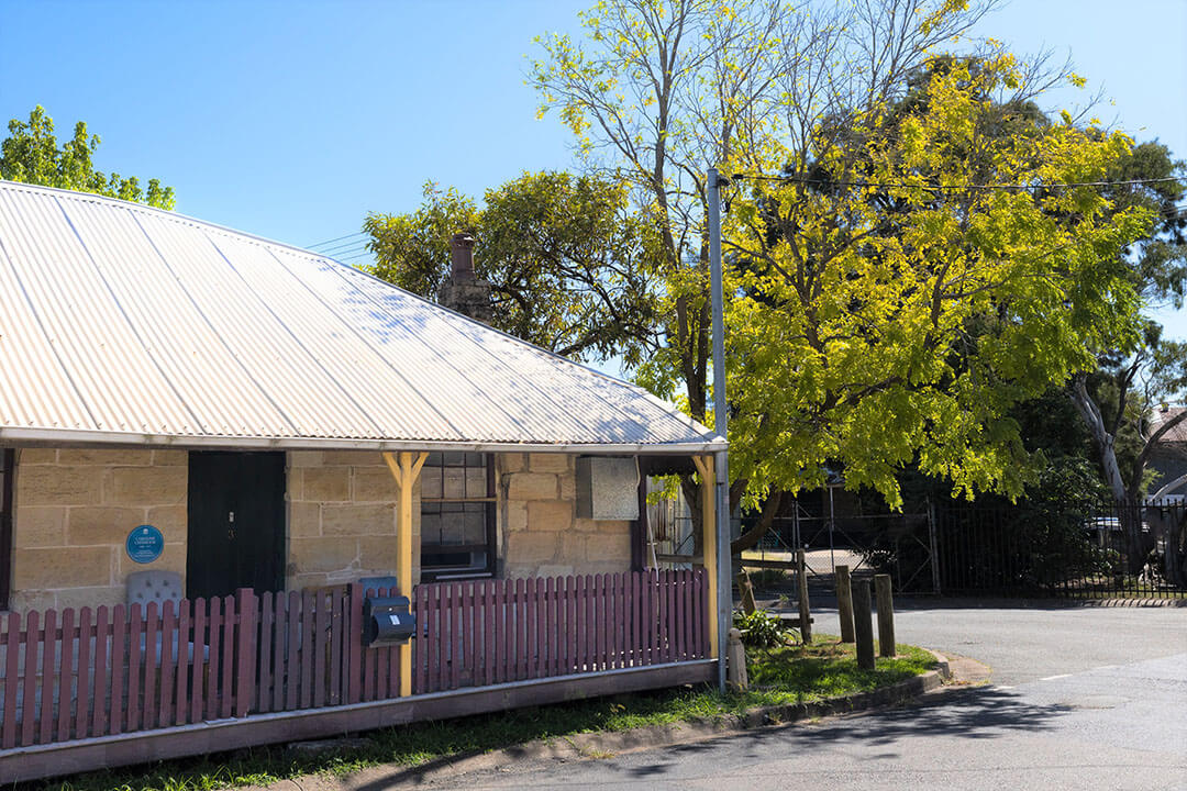 Photograph showing the property at 3 Mill Street, Caroline Chisholm Cottage, East Maitland, positioned on the left side of the image. A blue plaque engraved with Caroline Chisholm’s name is mounted on the wall of the cottage. The building features heritage-style architecture, and the plaque highlights its historical significance.