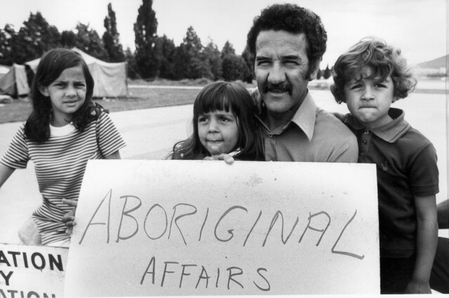 Black and white image of Charles Perkins and his children protesting outside. They are holding a sign that reads 'ABORIGINAL AFFAIRS'.