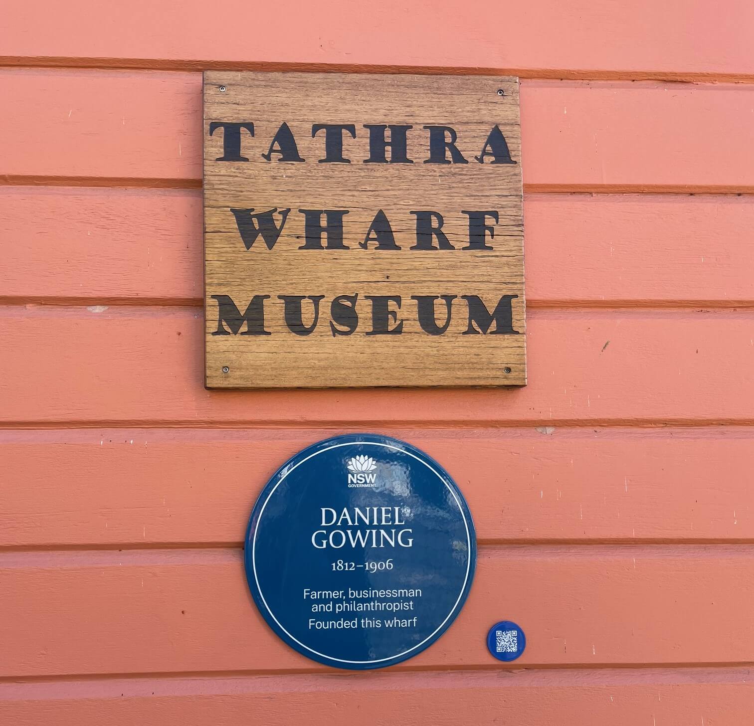 Blue Plaque commemorating Daniel Gowing, mounted on a brown wooden wall beneath the 'Tathra Wharf Museum' sign. The plaque reads: 'Farmer, businessman and philanthropist. Founded this wharf,' recognising Gowing’s role in establishing the Tathra Wharf.