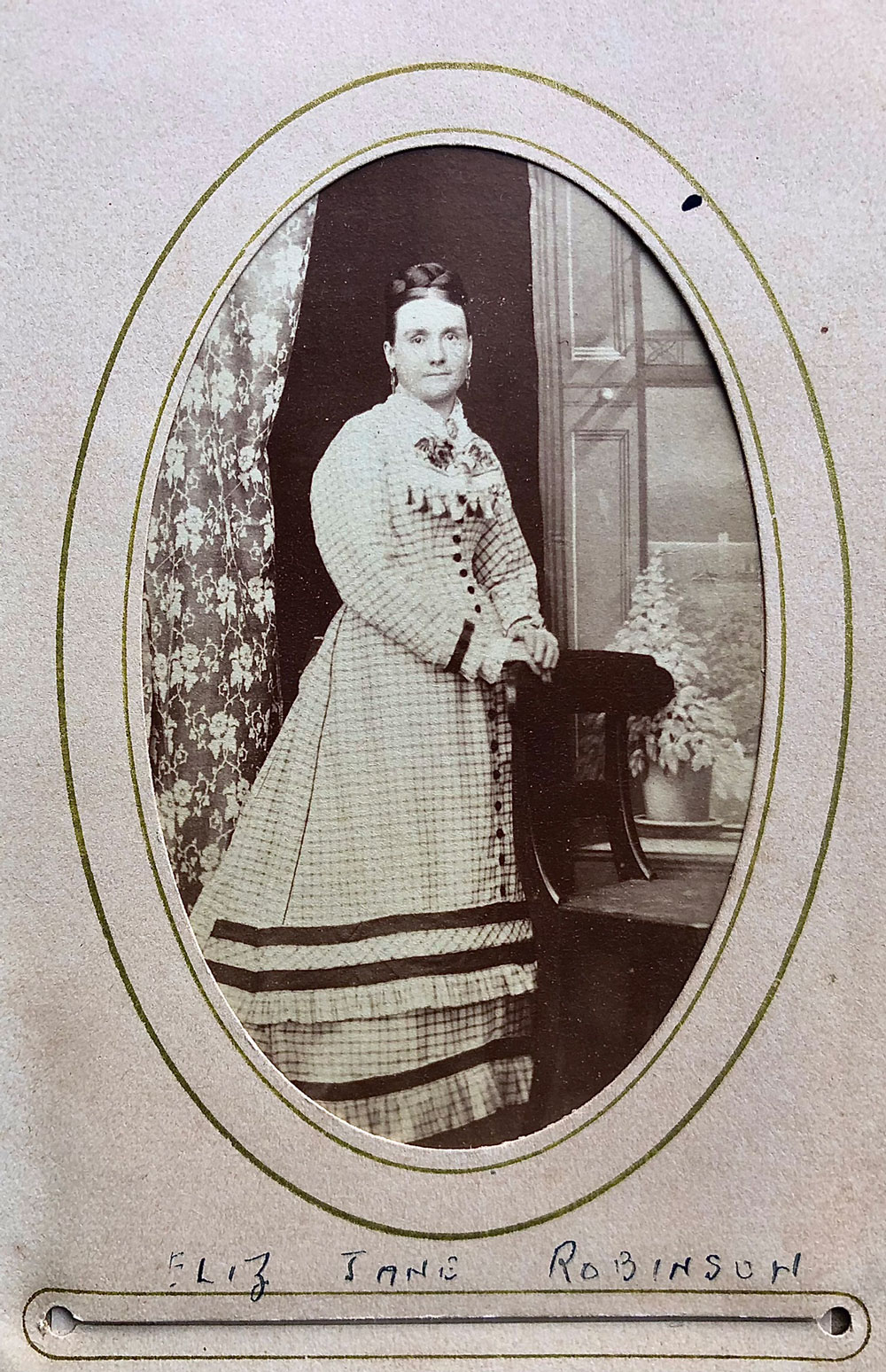 A formal portrait of Bessie Robinson wearing a light-coloured dress, standing next to a window.