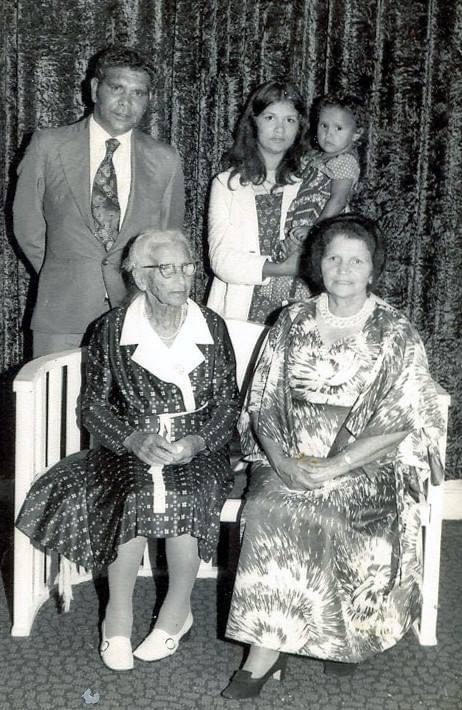 Black and white photograph of an elderly Emma Jane Callaghan seated in the front row alongside her daughter Kathleen Davison (deceased). Also in the front row is her grandson Leslie Davison (deceased), dressed in a suit and tie. Standing in the back row is great-granddaughter Mary Davison, holding her daughter Linda Davison (deceased). The multi-generational family portrait captures a moment of legacy and connection.