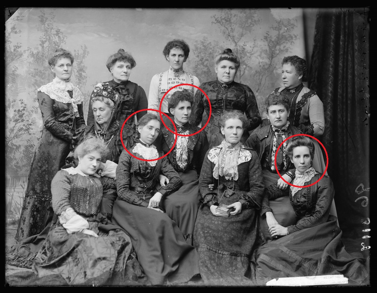 Image 2 of 3 - Black and white group photo of the Womanhood Suffrage League of New South Wales. 12 women are seated or standing in 3 rows all wearing full length dresses with long sleeves and updo hairstyles. Annie (centre row), Bella (2nd from left, front) and Kate (far right, front) Golding circled in the photo.