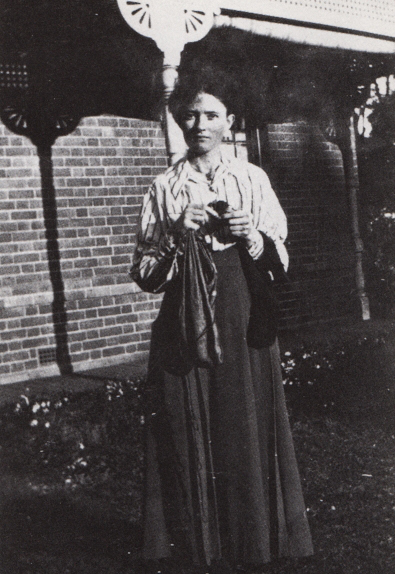 Black and white portrait of a woman standing outside wearing a shirt and a long skirt.